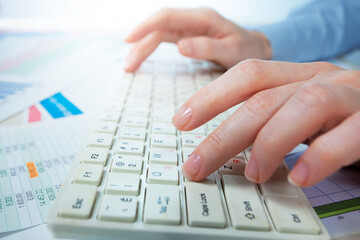A woman working on an accounting report with a computer. Close-up of her hands.
