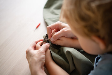 Mother seamstress with her baby sitting on her lap, together unpicking a seam on trousers. Top view of hands, motherhood and care.