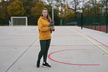 A sporty young woman with yoga mat in the stadium