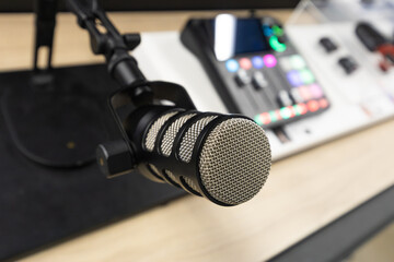 Podcast recording workspace with professional condenser microphone on adjustable stand and digital audio mixer with illuminated controls on a modern desk setup