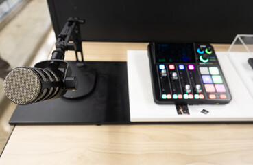 Podcast recording workspace with professional condenser microphone on adjustable stand and digital audio mixer with illuminated controls on a modern desk setup