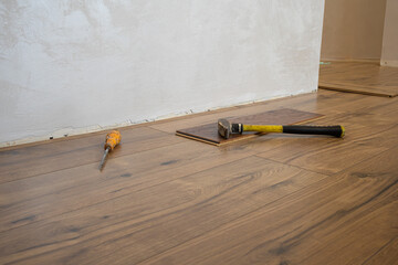 A hammer and screwdriver rest on a newly installed wooden floor in a living area during renovation. The walls are light-colored