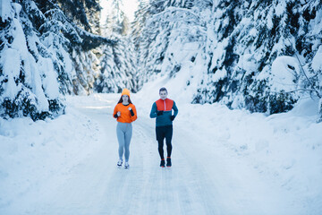 Young fit couple running through the snow in a park. Healthy winter lifestyle and motivation concept