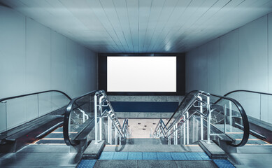 Symmetric view down metro escalators toward a large blank billboard screen mockup in a modern underground station, cool blue tones, copy space for advertising; wide-angle shot