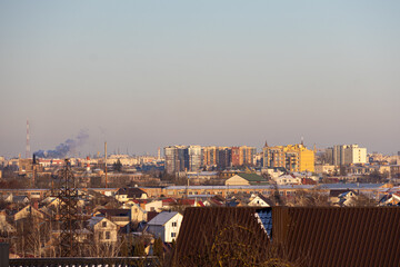 View looking over a city with many buildings, houses, and smoke from factories against a daylight sky