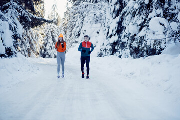 Young fit couple running through the snow in a park. Healthy winter lifestyle and motivation concept
