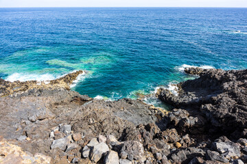 Emerald turquoise natural tide pool surrounded by jagged black volcanic rocks and endless blue ocean horizon at Costa El Sauzal, Tenerife, Canary Islands, Spain.