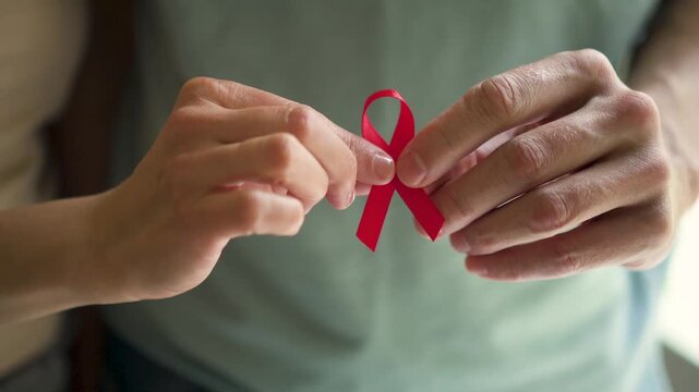 Mans hand carefully holding red satin ribbon symbolizing HIV AIDS awareness support for affected people and December hope.