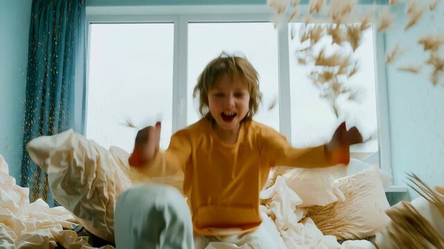 Energetic boy with messy hair jumping on a bed in slow motion. Feathers fly everywhere in a fun and chaotic bedroom scene. Carefree childhood and pure happiness