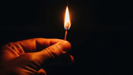 Burning matchstick held by hand in the dark, creating a warm glow.