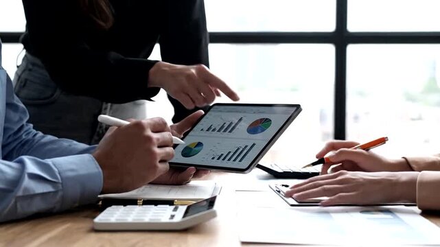 Close-up of three business colleagues collaborating, analyzing charts and graphs on a digital tablet in a bright, modern office setting. Focus on hands and data.