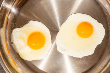 Two eggs frying in a stainless steel pan