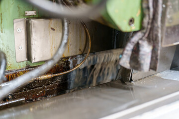 Machine part working with fluid in a workshop during daytime with metal and machinery visible around