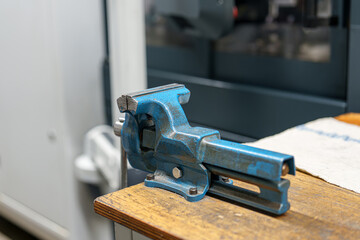 Metal tool placed on wooden table in workshop with machine in background during daytime