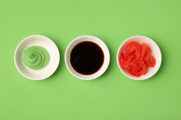 Bowls with wasabi, soy sauce and pickled ginger on green background