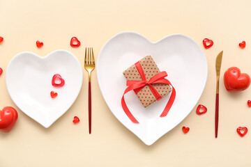 Table setting for Valentine's Day with gift box and decorative hearts on beige background