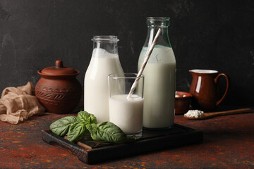 Bottles and glass of fresh kefir with basil leaves on dark table