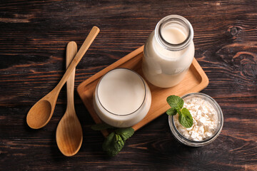 Glass of fresh kefir and jar of cottage cheese with mint on wooden background