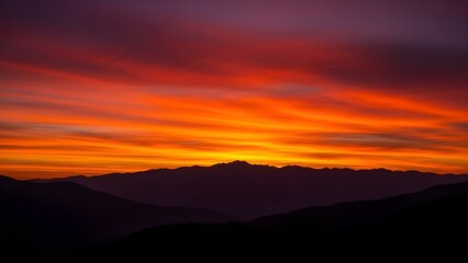 A vibrant sunset with fiery orange and purple clouds over dark mountain silhouettes.