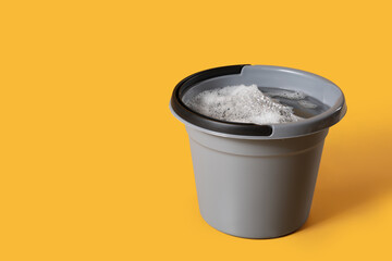 Plastic bucket with water and foam on yellow background © Pixel-Shot