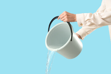 Woman pouring water from bucket on blue background