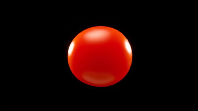 A single red cherry tomato against a stark black background showcasing its vibrant color and smooth texture