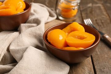Bowls with sweet canned peaches on wooden background, closeup