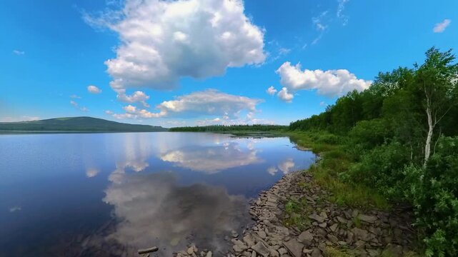 panoramic view of a calm lake surrounded by green trees and distant hills under a bright blue sky with fluffy white clouds, showcasing a perfect reflection on the water's surface. Ideal for nature, tr