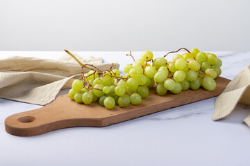 Cluster of green grapes on a well-lit wooden board.
