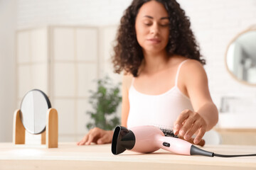 Beautiful young African-American woman with modern hair dryer at table in bathroom