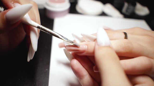 Manicure expert carefully leveling gel polish during extension procedure, creating smooth, even surface with professional technique.
