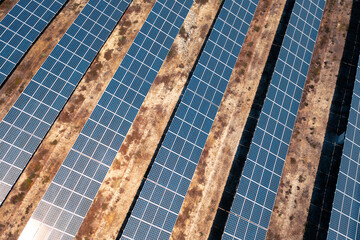 Overhead view of solar power plant featuring multiple rows of photovoltaic panels arranged on dry terrain producing clean renewable energy for sustainable development