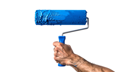 Close-up of a hand holding a paint roller with vibrant blue paint against black