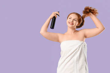 Beautiful young redhead woman applying hair spray on lilac background