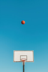 Basketball ball high above hoop with large copy space. Minimal outdoor sports concept.