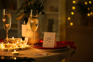 Beautiful table setting with roses, burning candles and greeting card at evening. Valentine's Day...