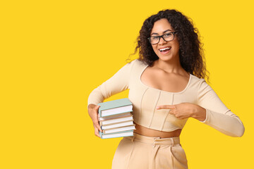 Young African-American woman pointing at books on yellow background