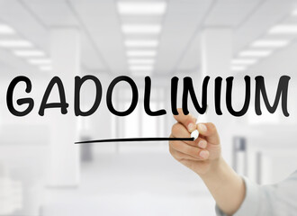 A conceptual image featuring the word "Gadolinium" handwritten in bold black letters on transparent glass, with a blurred modern white office in the background, representing this rare earth metal