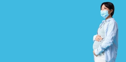 Pregnant Asian woman in medical mask on blue background with space for text