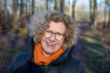 very attractive smiling senior woman in the forest with jacket in autumn
