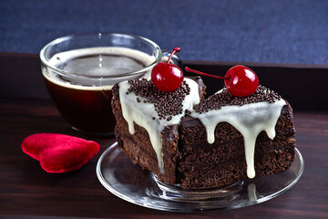 Celebratory chocolate cake with glaze and canned cherry, cup of coffee on the wooden tray.