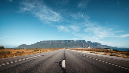 Fototapeta premium Empty highway leading to flat topped mountain under blue sky with wispy clouds