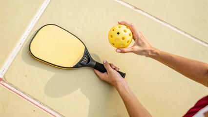 Hands holding pickleball paddle and ball on court