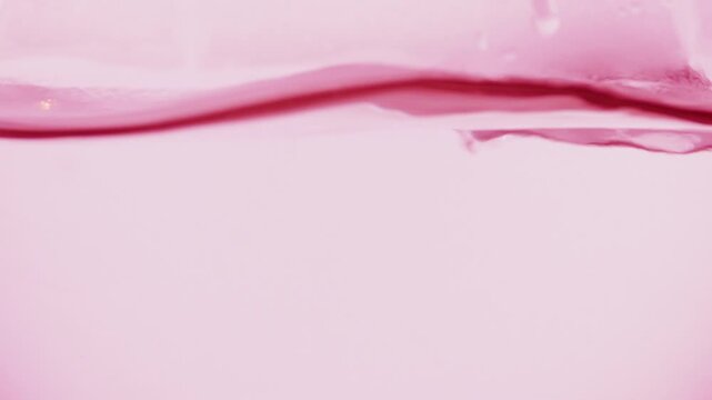 Macro shot of rosy transparent fluid boiling in a round-bottom flask, producing bubbles and waves on pale pink background