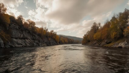 A river flows between rocky cliffs with autumn foliage under a cloudy sky