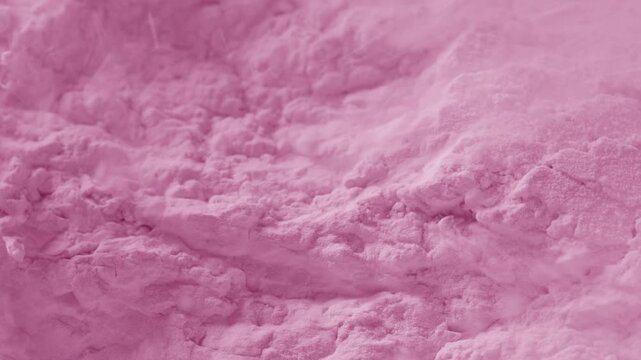 Detailed macro slow-motion recording of chipped pink powder surface being blown with a strong air stream, breaking its structure and chipping it into small pieces