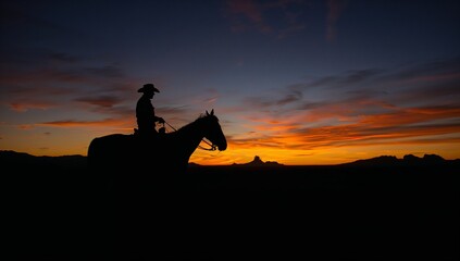 Silhouette of a cowboy on horseback against a dramatic sunset sky in the desert