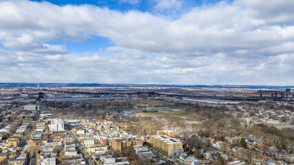 Aerial drone view over Lincoln Park in Jersey City with the Pulaski Skyway stretching across the horizon above the Hackensack River. Surrounding residential neighborhoods, open green space, and waterw