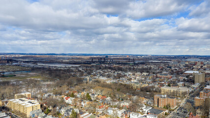 Aerial drone view over Lincoln Park in Jersey City with the Pulaski Skyway stretching across the horizon above the Hackensack River. Surrounding residential neighborhoods, open green space, and waterw