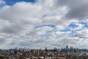 Aerial drone photo from Jersey City featuring Manhattan skyline views, dense city blocks, waterfront buildings, and modern New York City architecture under dynamic daytime cloud cover.                